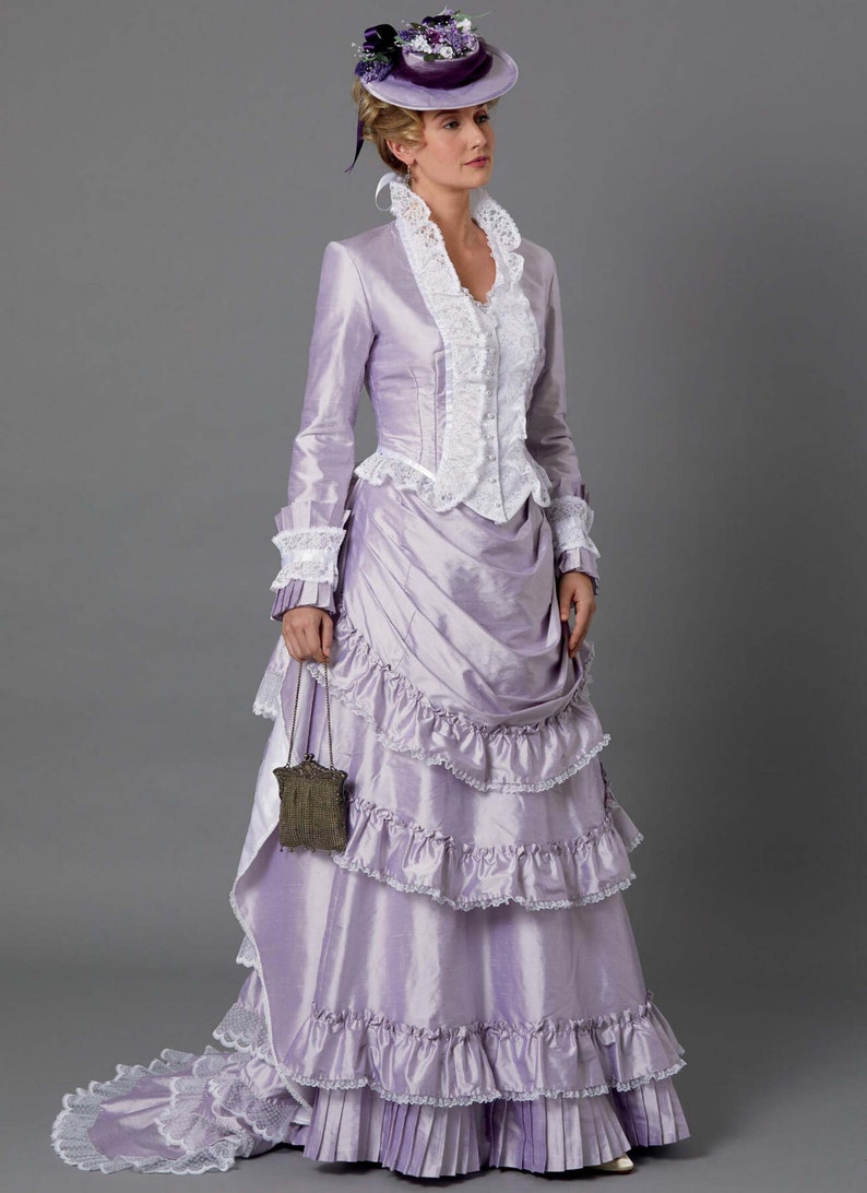 May include: A woman in a lavender dress with a white lace bodice and a ruffled skirt. She is wearing a small hat with purple flowers and a small purse.