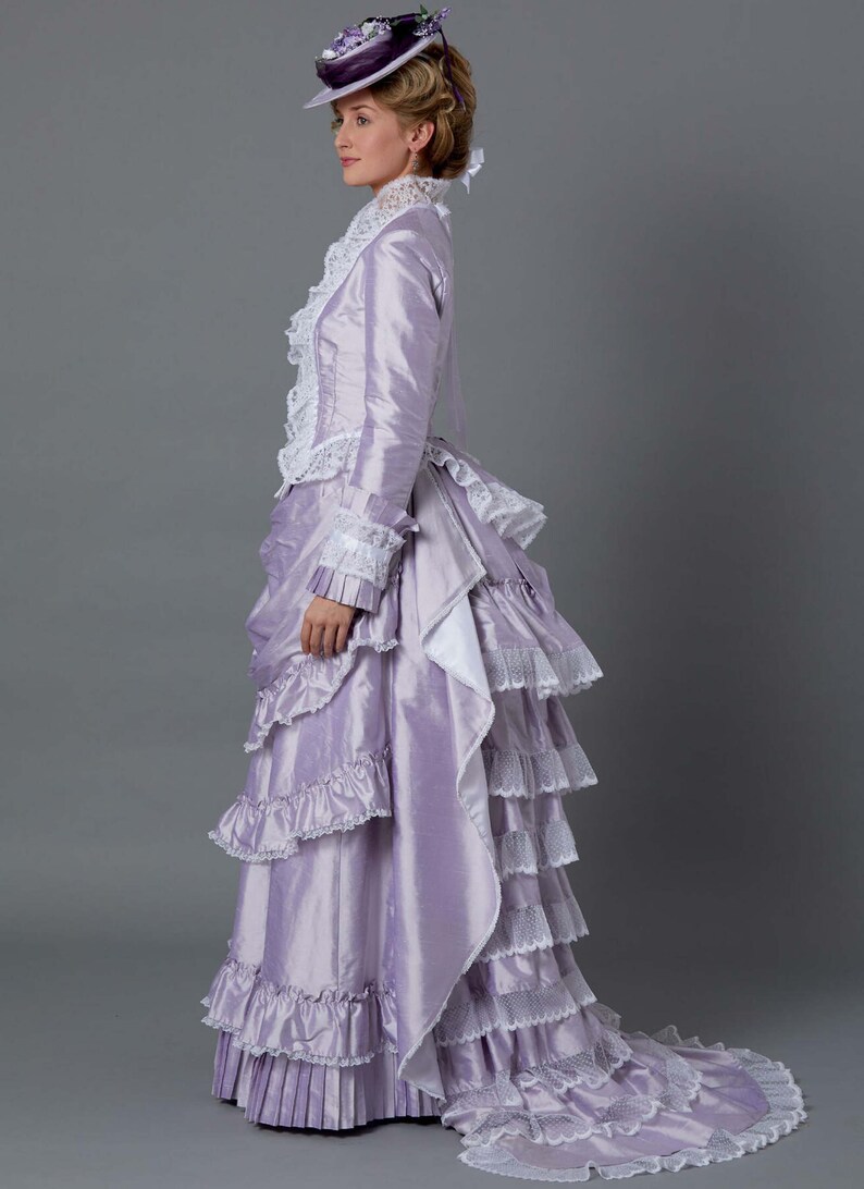 May include: A woman in a lavender dress with a white lace trim and a matching hat. The dress has a bustle in the back and a long train.