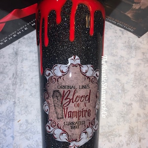Pu&ograve; includere: Un bicchiere nero glitterato con un design a goccia rosso nella parte superiore. Il bicchiere presenta un'etichetta con il testo "Blood of a Vampire" e un'illustrazione di bara. Un articolo da bere unico e a tema.