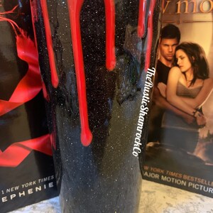 Pu&ograve; includere: Un bicchiere nero glitterato con gocce rosse, che ricordano il sangue. Il bicchiere ha il testo "The Rustic ShamrockCo" sul lato. Lo sfondo include le copertine dei libri "Twilight" e "New Moon" di Stephenie Meyer.