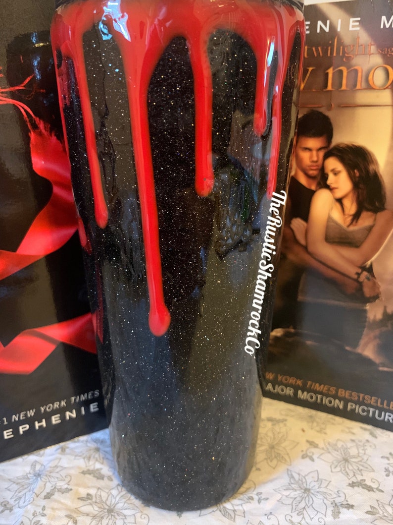 Pu&ograve; includere: Un bicchiere nero glitterato con gocce rosse, che ricordano il sangue. Il bicchiere ha il testo "The Rustic ShamrockCo" sul lato. Lo sfondo include le copertine dei libri "Twilight" e "New Moon" di Stephenie Meyer.