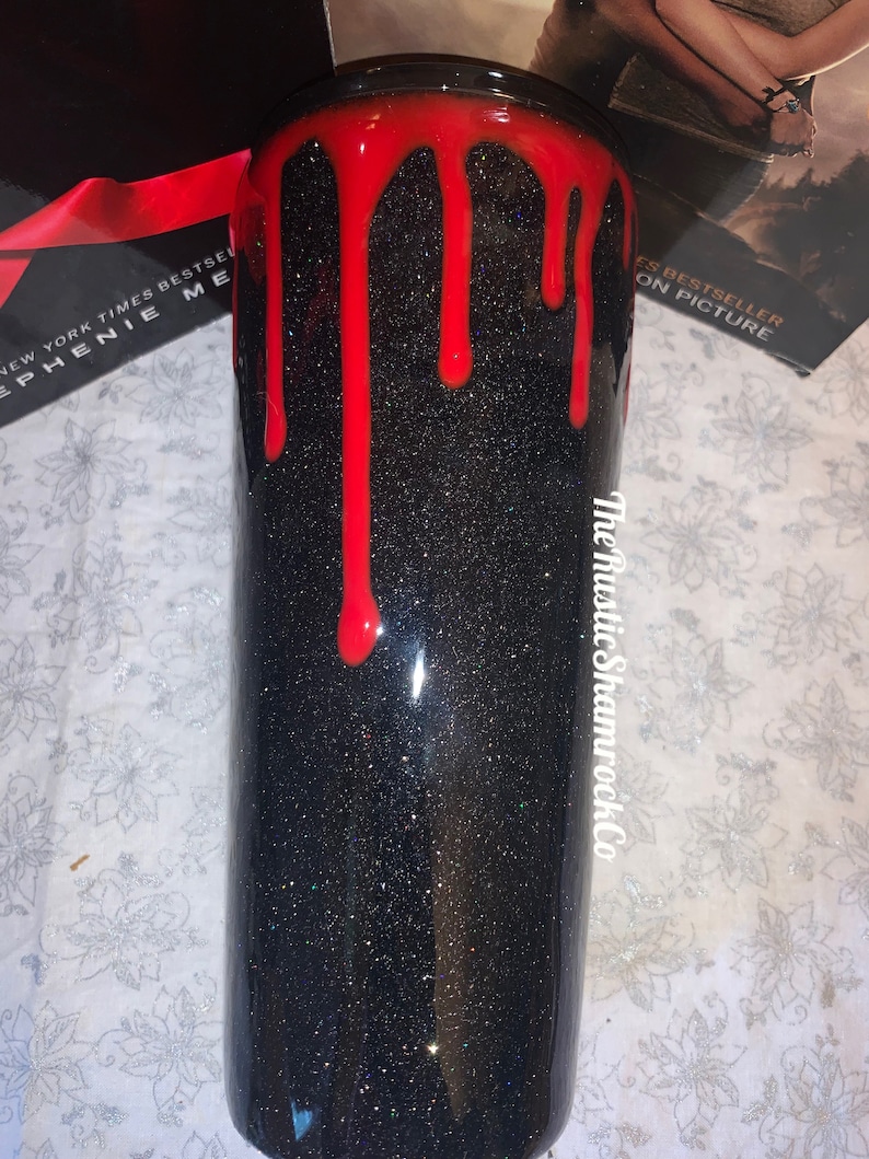 Pu&ograve; includere: Un bicchiere nero glitterato con un design di vernice rossa gocciolante. Il bicchiere ha una finitura lucida e il testo "The Rustic Shamrock Co" &egrave; visibile sul lato. Il bicchiere &egrave; cilindrico.