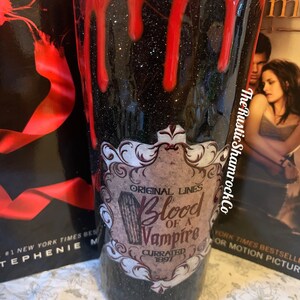 Pu&ograve; includere: Un bicchiere nero glitterato con gocce rosse sulla parte superiore. Il bicchiere presenta un'etichetta che recita "Original Lines Blood of a Vampire Currated 1897". The Rustic Shamrock Co.