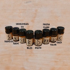 May include: Eight small glass bottles with black caps, each containing a brown liquid. Each bottle has a white label with a different symbol and text, including "Smoldering Ice", "Frozen Flame", "Senseless", "Rage", "Bliss", "Death", "Valor", and "Craze".