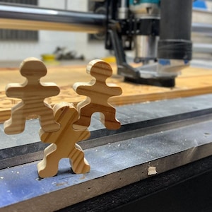 May include: Three wooden puzzle pieces shaped like people, stacked on top of each other. The pieces are made of light brown wood and have a simple, minimalist design.