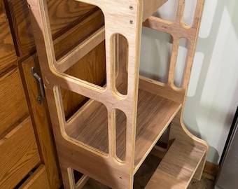 May include: A wooden step stool with two shelves and a step. The stool is made of light brown wood with a natural finish. It is designed to help children reach higher surfaces.