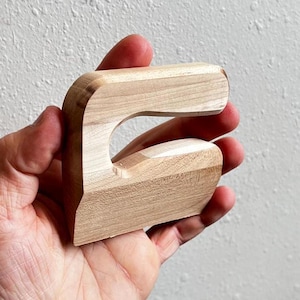 May include: A wooden hand-shaped tool with a curved opening, designed for woodworking.