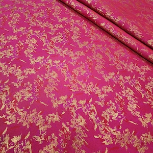 Op de afbeelding: Roze stof met een gouden bloemenpatroon. De stof heeft een textuur.