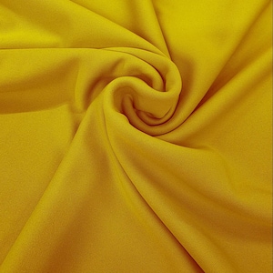 Puede incluir: Primer plano de una tela amarilla vibrante con pliegues suaves y una superficie texturizada. La tela está drapeada, creando una sensación de profundidad y movimiento. Las palabras "Daylin Fabrics" están impresas en la esquina inferior derecha.