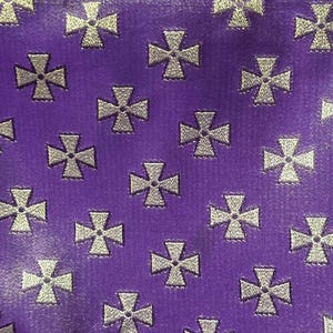 May include: Close-up of a purple fabric with a repeating pattern of silver crosses. The crosses are evenly spaced across the surface, creating a textured appearance. The fabric has a subtle sheen.