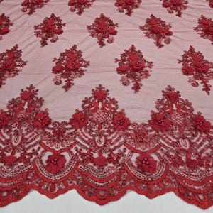 Puede incluir: Tela de encaje rojo bordada con diseños florales y ornamentales. La tela presenta aplicaciones de flores en 3D y detalles de cuentas. El borde festoneado añade un toque decorativo. Ideal para vestidos de novia, de noche o ropa de ocasión especial.