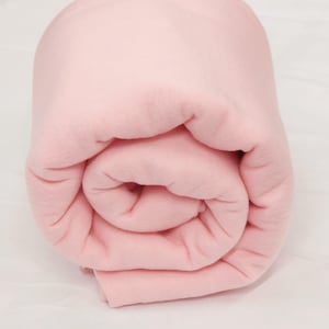 Può includere: Una morbida coperta di pile rosa arrotolata. La coperta è realizzata in un materiale morbido e soffice.