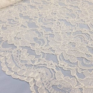 May include: White lace fabric with a delicate floral pattern. The lace has a scalloped edge.