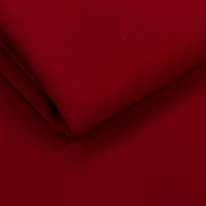 Puede incluir: Primer plano de una tela roja oscura doblada. La tela tiene una textura suave y un color rico y saturado. Los pliegues crean sombras y reflejos, añadiendo profundidad a la imagen. La tela parece ser de color liso.