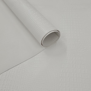 Puede incluir: Un rollo de piel sintética blanca con un patrón texturizado de piel de cocodrilo. El material está parcialmente desenrollado, revelando una parte inferior blanca mate y lisa, y una superficie superior estructurada y en relieve con un patrón de escamas.