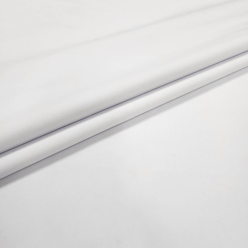 May include: White fabric with a smooth texture. The fabric is folded in half, creating a crease down the center.