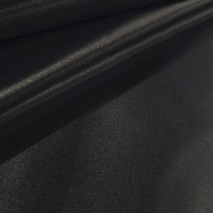 May include: Close-up of black fabric with a subtle sheen. The material is folded, creating soft shadows and highlights that emphasize the texture. The fabric appears smooth and possibly silky.