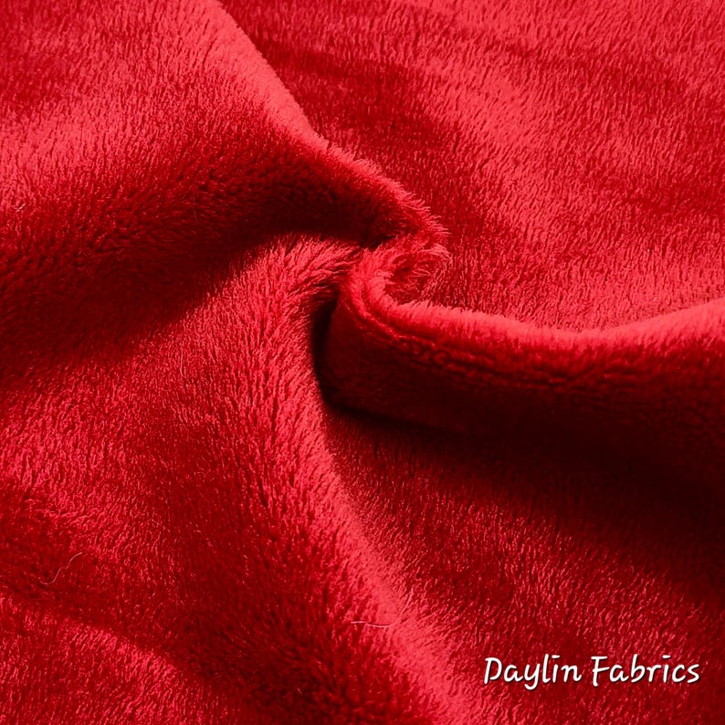 May include: Close-up of a soft, red fabric with a fuzzy texture. The fabric is folded in half, showing the inside and outside of the material. The text "Daylin Fabrics" is visible in the bottom right corner.