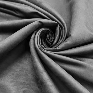 Può includere: Primo piano di un tessuto grigio dalla texture morbida e vellutata. Il tessuto è drappeggiato e arricciato, creando un motivo a spirale al centro. Le pieghe e le ombre aggiungono profondità e dimensione al materiale.