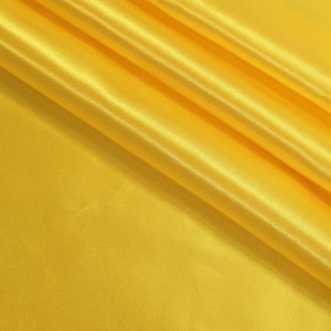 May include: A length of bright yellow satin fabric featuring a smooth, lustrous surface with a reflective sheen. The material is draped in soft, diagonal folds that create subtle highlights and shadows across the vibrant, solid-colored textile.