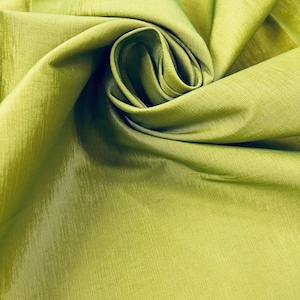 Puede incluir: Primer plano de una vibrante tela verde lima con un brillo sutil. El material está elegantemente drapeado y arremolinado, creando un efecto texturizado y en capas. La superficie de la tela tiene una fina apariencia tejida, lo que sugiere un textil de alta calidad.