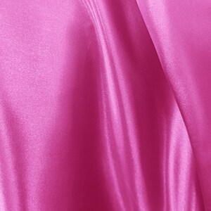 May include: Close-up of a vibrant pink satin fabric. The fabric is draped, creating soft folds and shadows. The smooth, shiny surface reflects light, highlighting the texture and color of the material.
