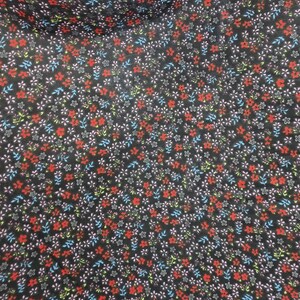 May include: Close-up of a black fabric covered in a repeating floral pattern. The flowers are small and feature red, white, blue, and green accents. The fabric has a slightly wrinkled texture.