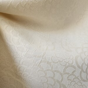 May include: Close-up of a cream-colored fabric with a subtle embossed floral pattern. The fabric has a soft, textured surface.