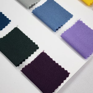 May include: A collection of fabric swatches in various colors, including dark green, purple, light blue, and lavender. The swatches are arranged on a white surface.