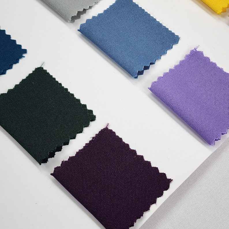 May include: A collection of fabric swatches in various colors, including dark green, purple, light blue, and lavender. The swatches are arranged on a white surface.