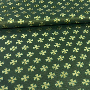 May include: Dark green fabric with a repeating pattern of gold crosses. The fabric is folded, showing the texture and sheen of the material. The gold crosses are evenly spaced across the surface, creating a decorative design.