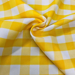 Puede incluir: Primer plano de una tela a cuadros amarillos y blancos. La tela está doblada, mostrando el patrón de grandes cuadrados. Los colores amarillo brillante y blanco crean un aspecto clásico y alegre, adecuado para diversos proyectos de artesanía y decoración del hogar.