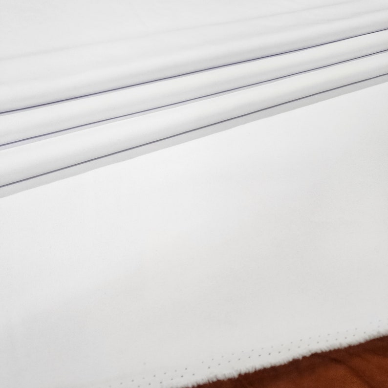 May include: White fabric with a subtle sheen and a fine, dotted edge. The fabric is folded in thirds, creating a smooth, clean surface.