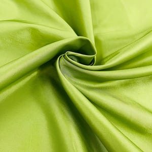 Puede incluir: Primer plano de una tela verde lima vibrante con un brillo sedoso. La tela está drapeada y doblada, creando sombras y reflejos suaves. El material parece suave y lujoso, adecuado para ropa o decoración del hogar.
