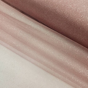 May include: Two rolls of pink tulle fabric with silver glitter. The fabric is sheer and has a delicate texture.
