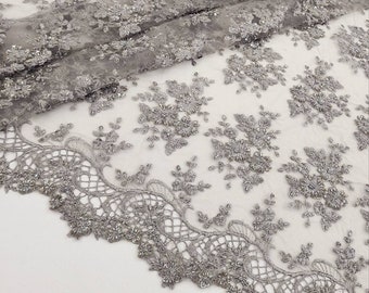May include: Silver beaded lace fabric featuring a delicate floral design. The lace has a scalloped edge and is ideal for adding a touch of elegance to any project.