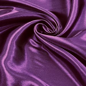 May include: Close-up of a luxurious, deep purple satin fabric. The fabric is draped and folded, creating a swirling pattern with highlights and shadows. The smooth, shiny material reflects light, showcasing its rich color and texture.