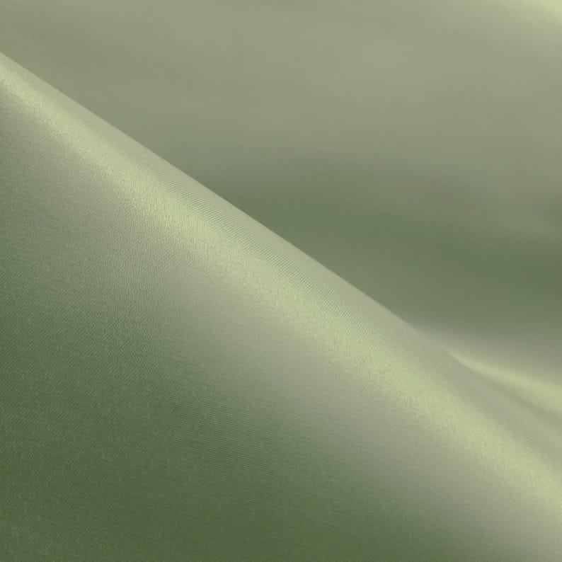 May include: Close-up of a sage green fabric with a subtle sheen. The material is folded, creating soft shadows and highlights. The texture appears smooth and luxurious, suggesting a high-quality textile.