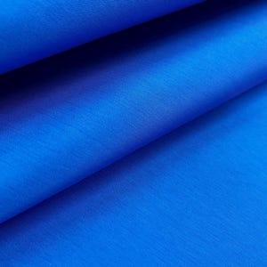 May include: Close-up of vibrant blue fabric with visible texture and folds. The material appears to be a smooth, woven textile, possibly used for clothing or home decor. The bright color and subtle sheen suggest a high-quality material.
