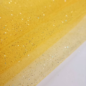 Könnte beinhalten: Gelber Tüllstoff mit schimmerndem Glitzer. Der Stoff ist in der Mitte gefaltet, so dass der Glitzer auf beiden Seiten sichtbar ist.