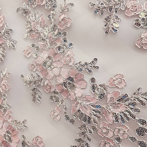 May include: Pink and silver floral lace fabric with a delicate pattern. The fabric is sheer and has a soft, romantic feel.