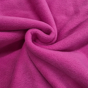 May include: Close-up of a vibrant fuchsia fleece fabric. The soft, textured material is folded and draped, creating shadows and depth. The fabric is a solid color, with the words "Daylin Fabrics" in white at the bottom.