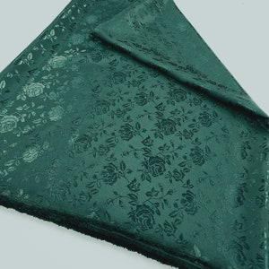 Könnte beinhalten: Ein tiefgrüner Stoff mit einem erhabenen Blumenmuster aus Rosen. Der Stoff hat eine weiche, samtige Textur.