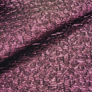 May include: Close-up of a pink and black textured fabric with a metallic sheen. The fabric has a geometric pattern.