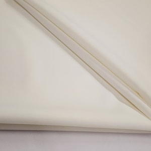 May include: Off-white fabric with soft folds. The fabric appears to be a smooth, lightweight material, possibly linen or a similar textile. The folds create shadows and add depth to the image.