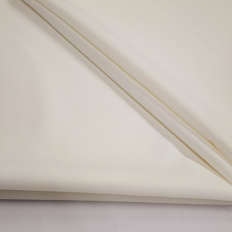 May include: Off-white fabric with soft folds. The fabric appears to be a smooth, lightweight material, possibly linen or a similar textile. The folds create shadows and add depth to the image.
