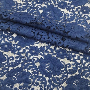 May include: A close-up of a blue lace fabric with a floral pattern. The lace is delicate and intricate, with a soft, flowing texture.