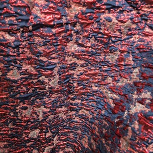 May include: Close-up of a textured fabric with a metallic sheen. The fabric has a blue base with red and gold accents.