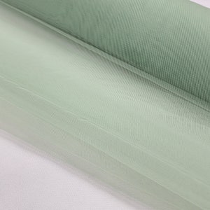May include: A roll of light green tulle fabric. The fabric is soft and sheer, with a delicate texture.