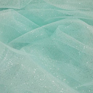 May include: A close-up of a light blue tulle fabric with silver glitter. The fabric is soft and delicate, and the glitter adds a touch of sparkle.